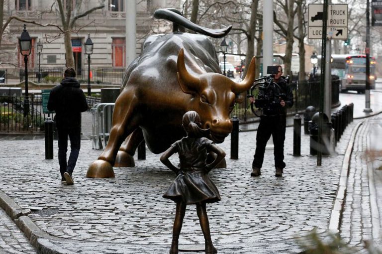 Estatua de una niña intrépida se posa frente al toro de Wall Street